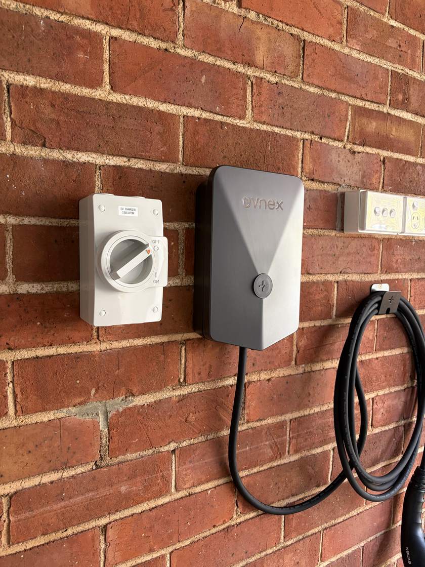 A weatherproof rotary isolator mounted beside the same Evnex charger, its cover engraved EV CHARGER ISOLATOR and marked off and on, so the charger circuit can be switched off at the charger itself