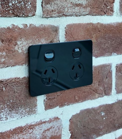 A matching black double powerpoint on the same brickwork, sitting flush and square, its finish matched to the scene controller nearby