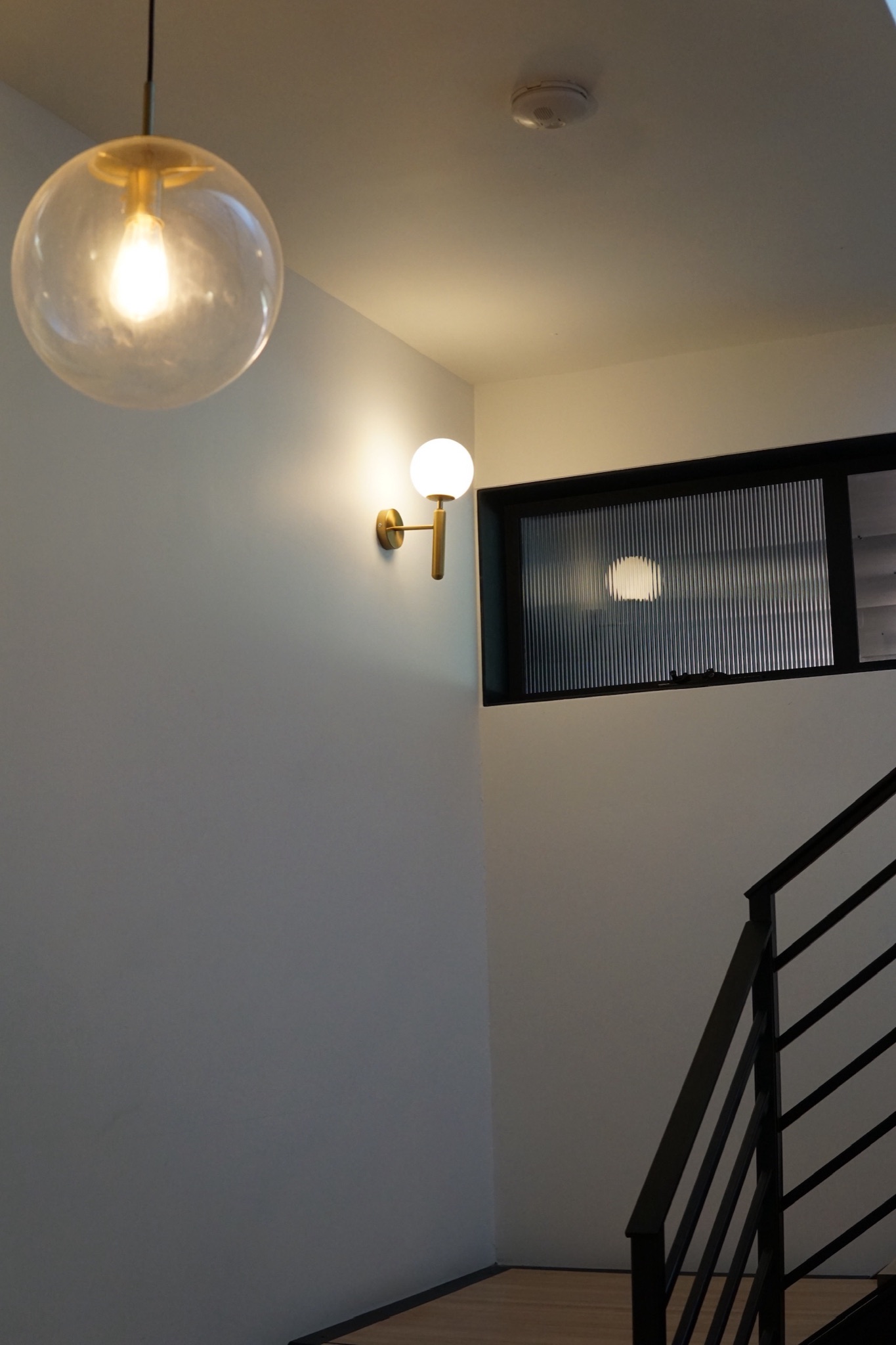 Layered stairwell lighting at dusk, glass globe pendant and wall sconce