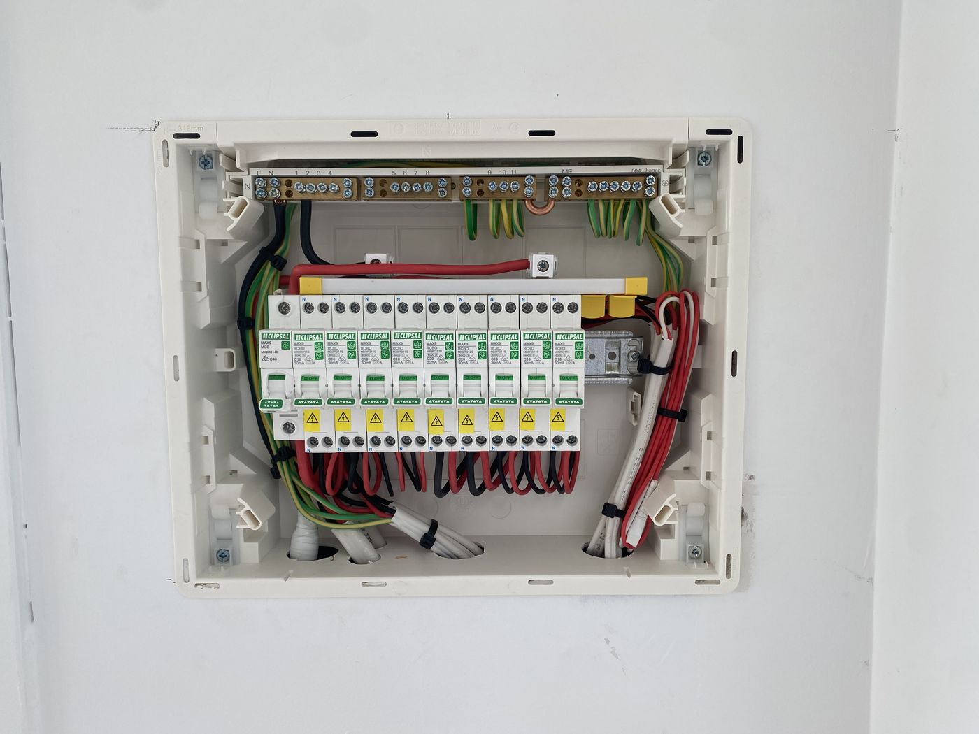 An East Arc Group switchboard with the cover off, showing a main switch and a row of ten Clipsal MAX9 RCBOs linked by a comb busbar, the neutral and earth bars landed above them, and every cable looped, dressed and cable tied in line